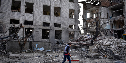 En person sopar undan bråte vid en byggnad i Zaporizjzjaregionen som skadats i ett ryskt luftanfall. Bild tagen i april.
