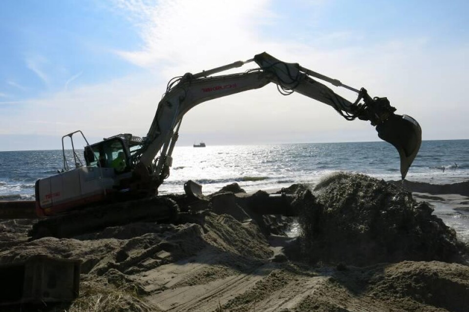 Grävmaskinistens uppgift är att styra sand- och vattenmassorna som forsar ut från pipelinen och fördela sanden på stranden. I solglittret 1 200 meter utanför ligger fartyget Magni I, som tömmer sin last via pipelinen på mindre än en halvtimme.