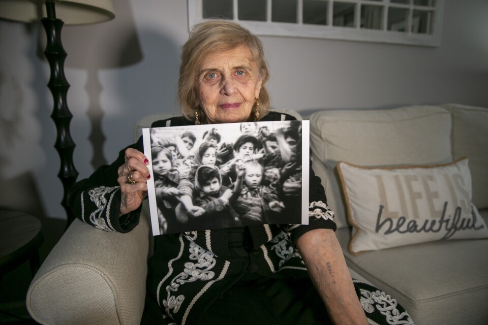 Överlevaren Tova Friedman, 85, i New Jersey USA, visar sin lägertatuering på armen och håller fram ett foto av henne och andra barn i Auschwitz vid befrielsen 1945.