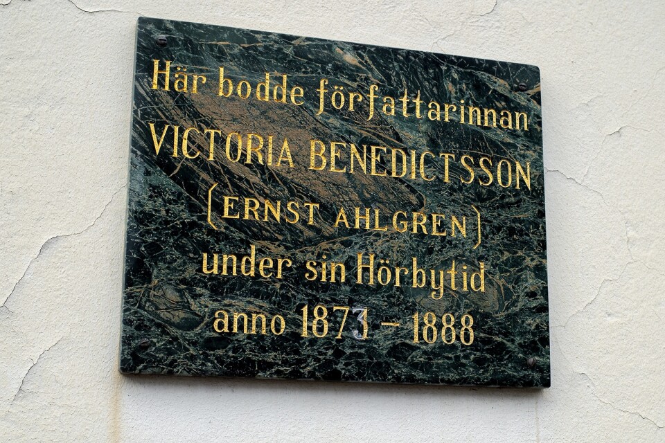 Minnesskylt över Victoria Benedictsson på husväggen i Hörby.