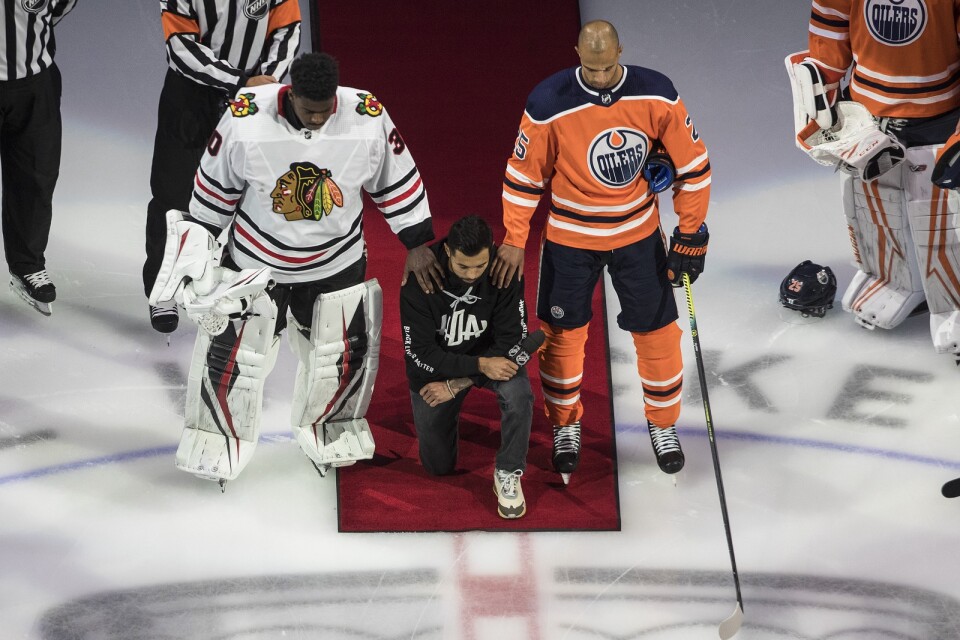 Minnesotas Matt Dumba knäböjer under USA:s nationalsång, flankerad av Chicagos Malcolm Subban och Edmontons Darnell Nurse, när NHL inledde playoffserien med att markera mot rasism.