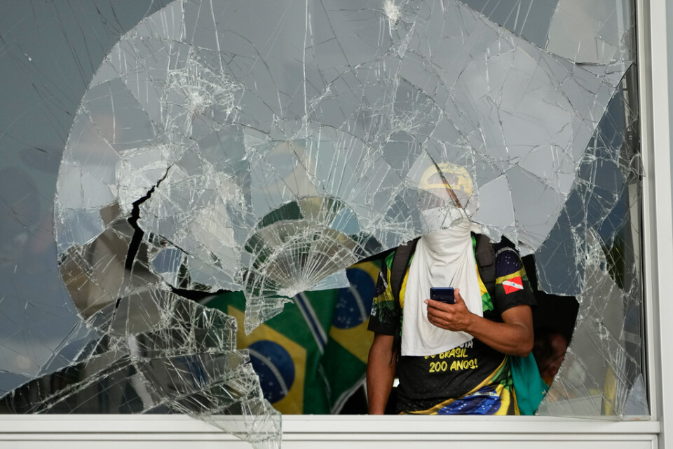 En anhängare till Jair Bolsonaro tittar ut genom ett krossat fönster i Planaltopalatset, den brasilianska presidentens kansli, under stormningen.