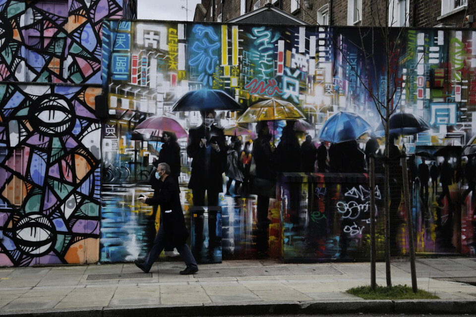 En man med munskydd går förbi en vägg i London. Arkivbild.