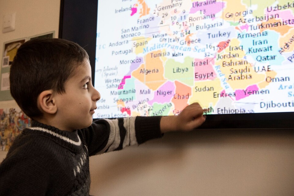 Yazan Esteila, som ännu inte lärt sig så mycket svenska, pekar på sitt hemland Syrien på förskolebibliotekets tv.