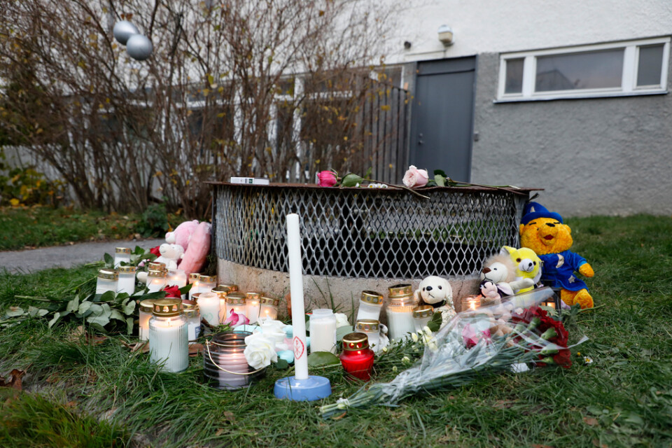 Gosedjur, blommor och ljus har lagts ner vid den plats där två barn hittades med livshotande skador utanför ett bostadshus i Hässelby i söndags kväll. Ett av barnen avled senare av sina skador. Tillståndet för det andra barnet är fortfarande allvarligt.