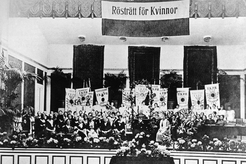 Landsföreningen för kvinnans politiska rösträtt (LKPR) har segermöte i Musikaliska akademien 1921 med högtidstal av Ellen Key. Palmer, blommor och standar från hela landet smyckar lokalen. Arkivbild.