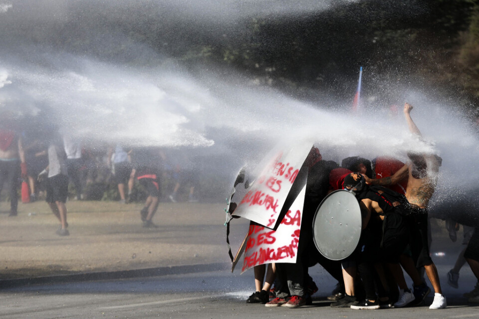 Regimkritiska demonstranter står emot trycket från vattenkanonerna i Chiles huvudstad Santiago den 15 november.