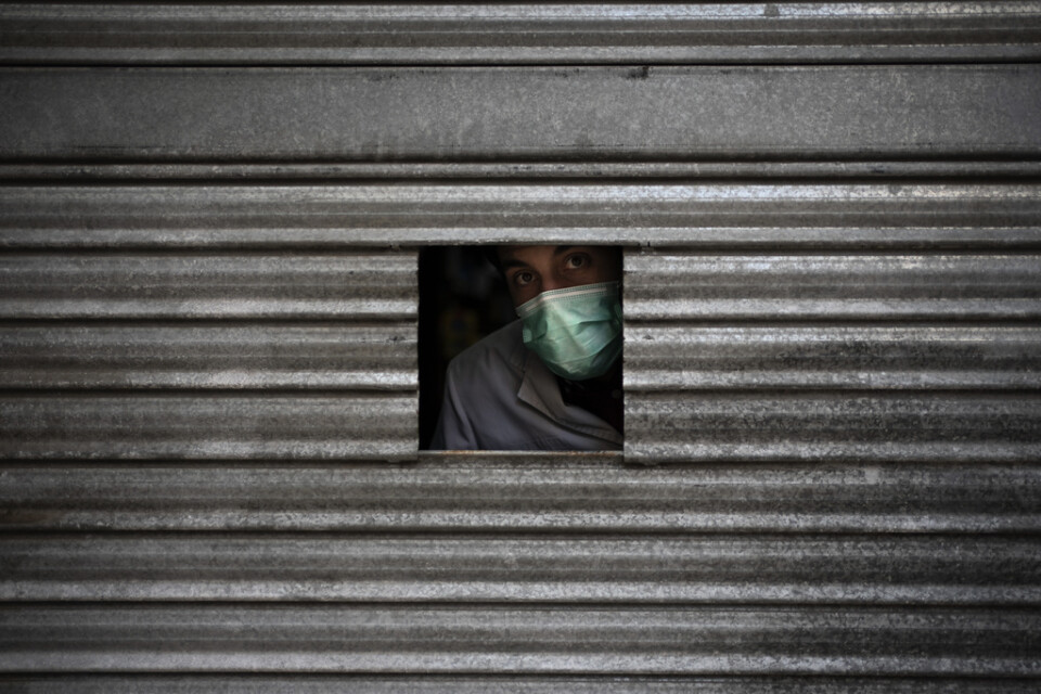En apoteksanställd blickar ut från en liten öppning i järnjalusin medan han inväntar kunder i Igualada i Katalonien.