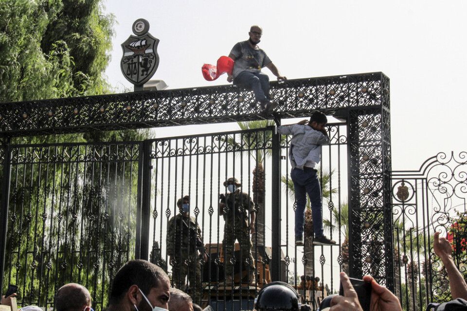 Tunisiska soldater vaktar huvudentrén till parlamentsbyggnaden i Tunis medan demonstranter samlas utanför.