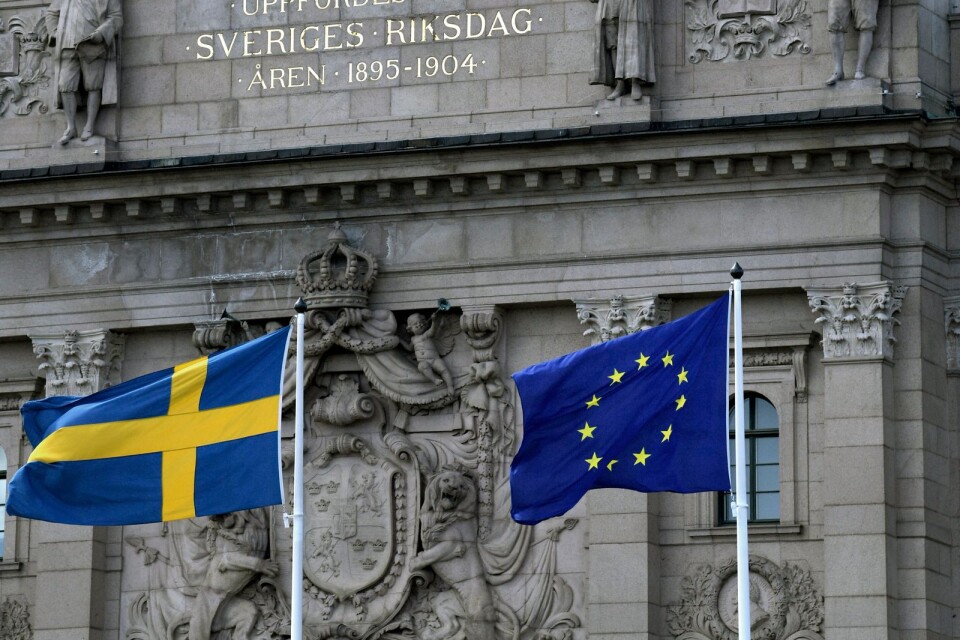 Riksdagshuset med svenska flaggan och EU-flaggan. Men EU ska låta bli den svenska modellen som fungerar bra utan inblandning utifrån.