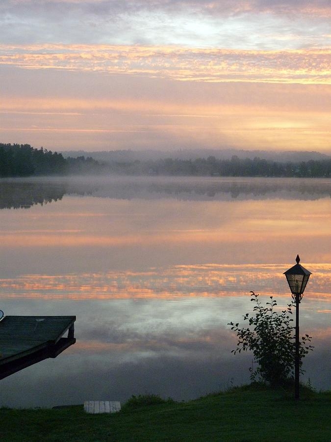 Den här bilden tog Karin Janson från sitt köksfönster en tidig morgon under sensommaren. Sjön låg spegelblank och i horisonten höll dimman just på att lätta.