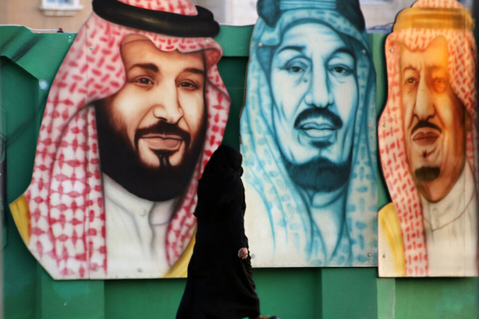 En kvinna passerar en bild som bland annat föreställer Saudiarabiens kung Salman (till höger) och kronprins Mohammed bin Salman (till vänster). Arkivbild.