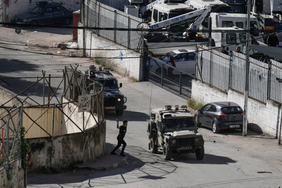 En palestinsk man kastar sten mot en konvoj med israeliska militärfordon under torsdagens räd mot Nablus.