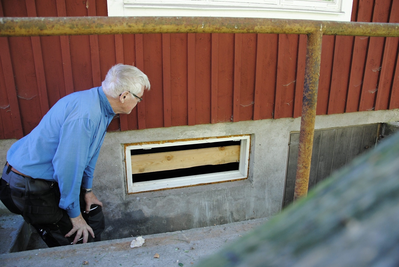 Sven Arnebranth visar ett källarfönster som har förstörts. En planka har tillfälligt fått ersätta fönstret.