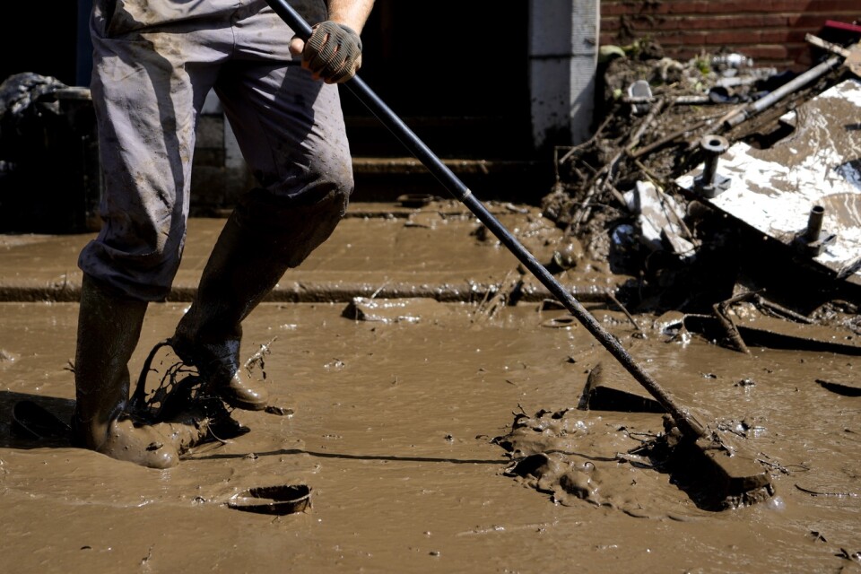 En invånare i belgiska Drolenvol svabbar undan lerigt vatten från de svåra översvämningarna. Arkivbild från den 17 juli.