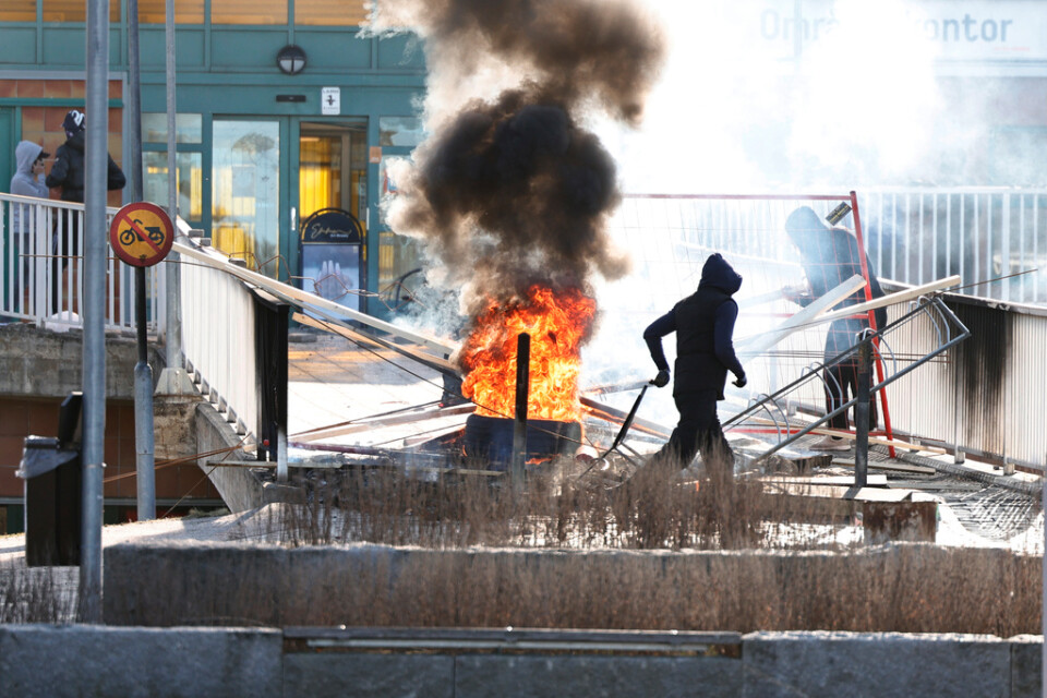 Personer gör en barrikad med brinnade bildäck och andra föremål vid Ringdansen centrum, i samband med upploppet i Navestad i Norrköping under påskdagen 2022. Arkivbild.