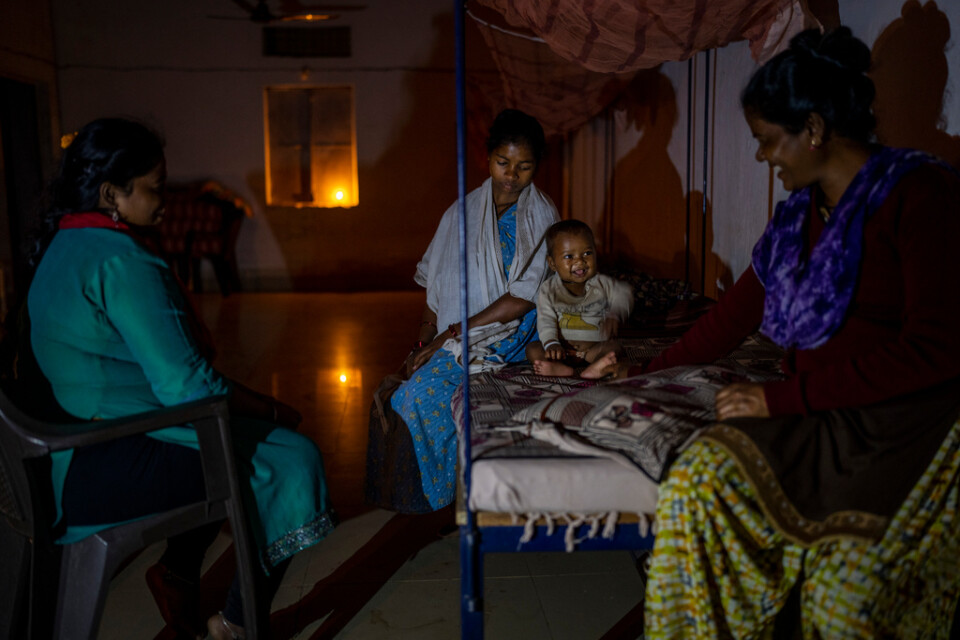Phagni Poyam och hennes son sitter på en säng på centret för gravida kvinnor. De två andra kvinnorna arbetar på centret.