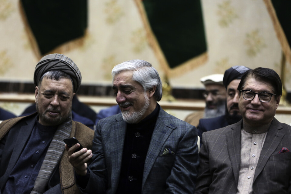 Den afghanske presidentkandidaten Abdullah Abdullah (mitten) reagerar på något han ser på sin telefon vid en presskonferens på söndagen.
