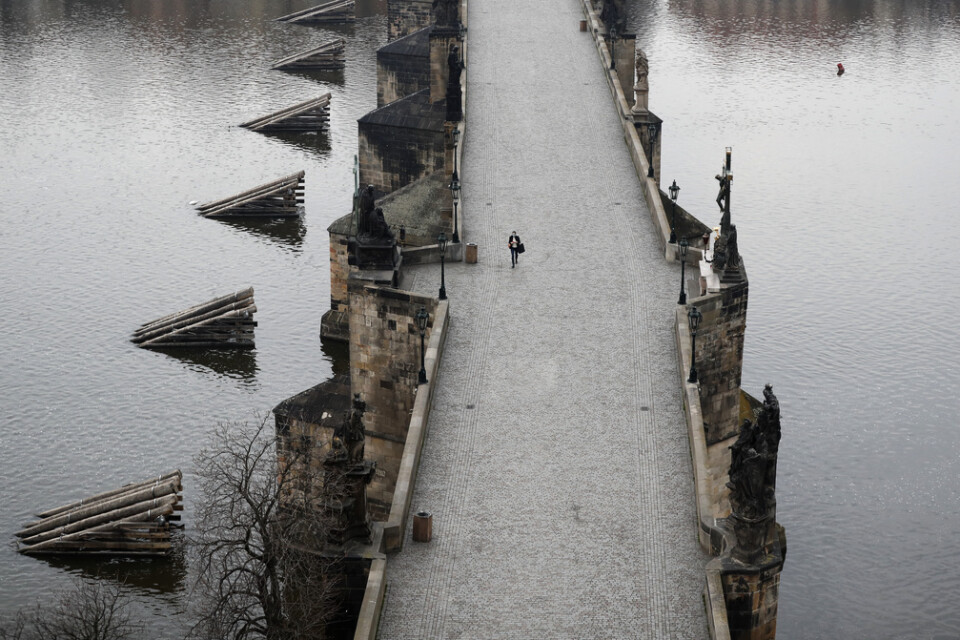 En kvinna promenerar över en nästintill tom Karlsbro i Prag i mars.