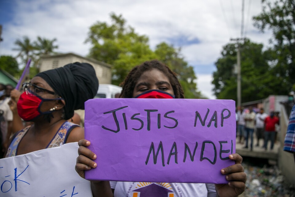 En kvinna utanför en rättsal i Croix-des-Bouquets håller upp en skylt med texten "Vi ber om rättvisa", på haitisk kreol, i samband med utfrågningarna den 14 maj av Yves Jean-Bart, Haitis fotbollsförbunds ordförande, som anklagas för sexuella övergrepp mot flera spelare.