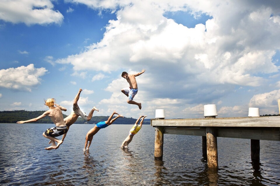 Glada ungdomar som hoppar från bryggan vid Skotteksbadet.