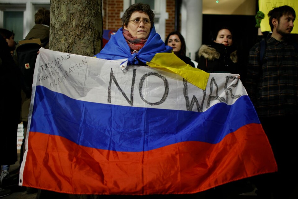 En kvinna med den ryska och ukrainska flaggan demonstrerar i Storbritannien. En av många globala protester till stöd för Ukraina under helgen.