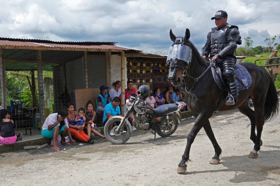 En ridande polis passerar människor som väntar utanför Bellavista-fängelset i Ecuador för att få information om sina anhöriga.