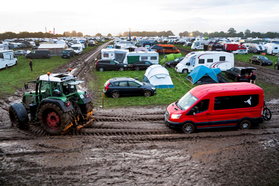 Bilar som kört fast i lerkaoset på festivalområdet får hjälp av traktorer att komma loss.