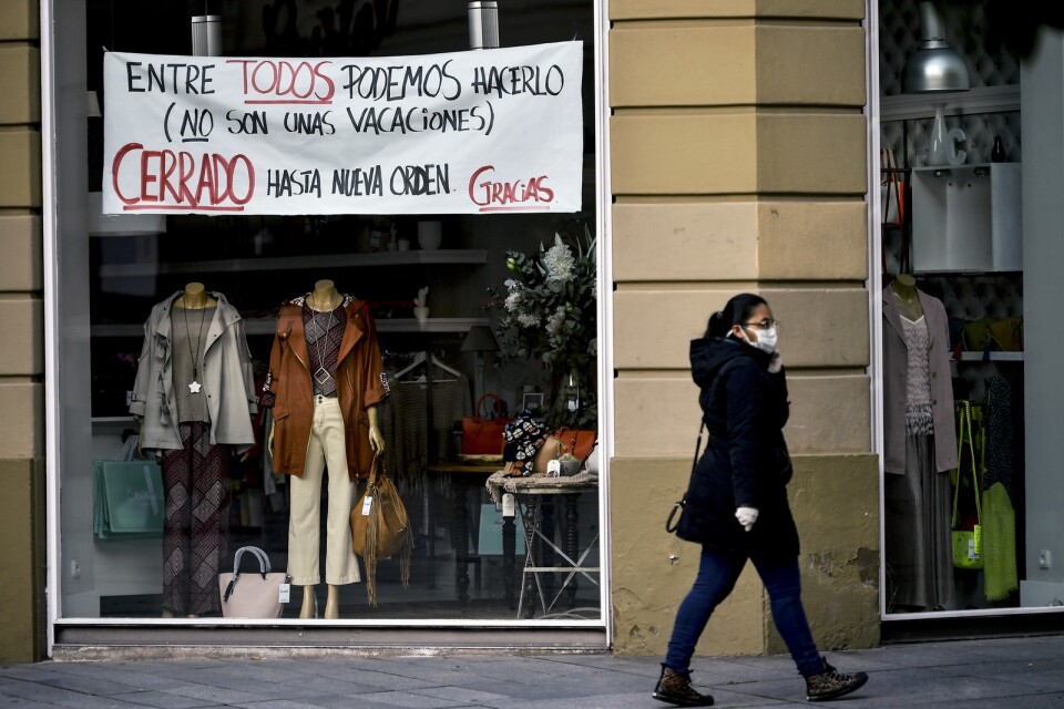 En kvinna med skyddsmask vid en stängd butik i spanska Pamplona.