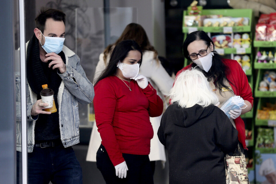 En anställd på en livsmedelsaffär delar ut masker till kunder i Wien i Österrike. Från onsdagen gäller masktvång i butiker.