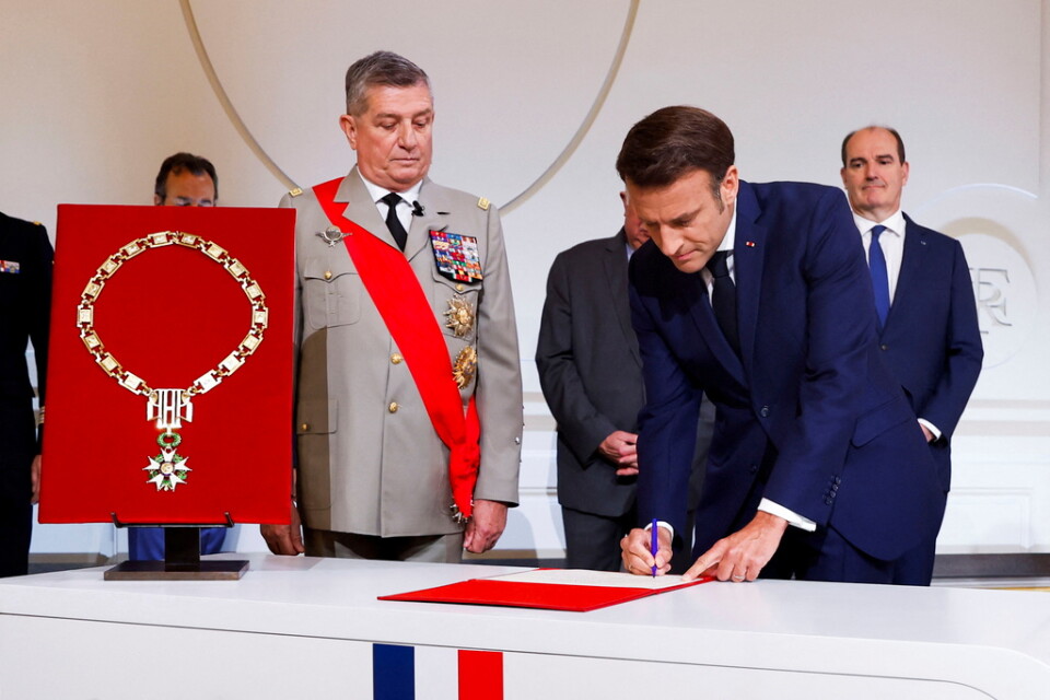 Emmanuel Macron skriver under pappren. Intill honom står militärens stabschef Benoît Puga.