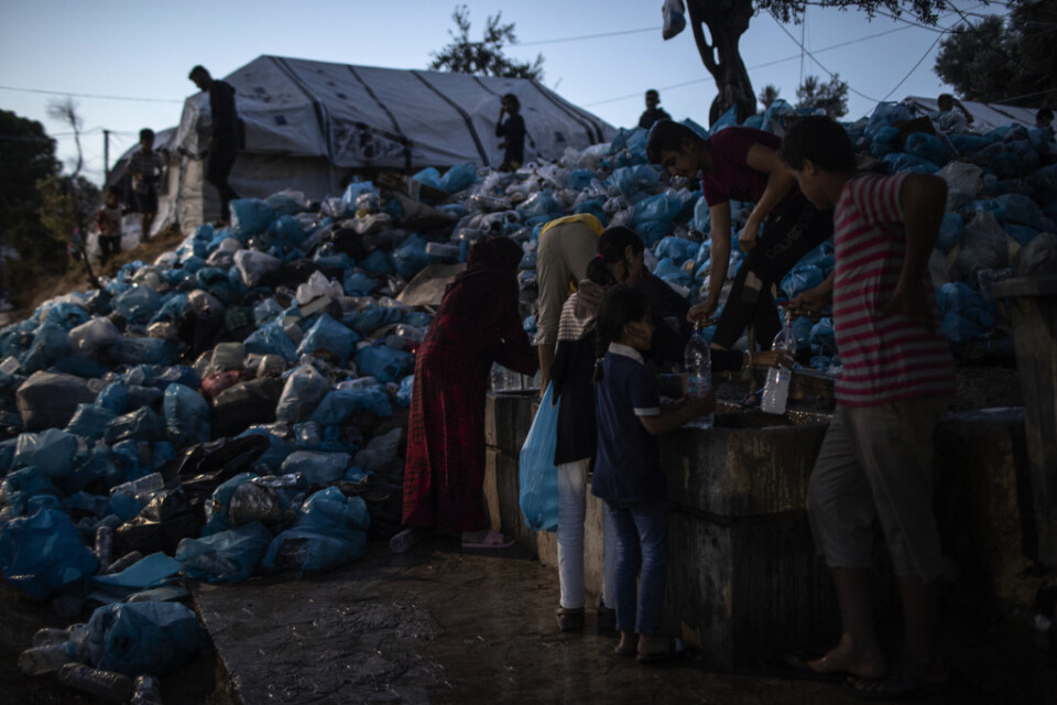 Människor i ett migrantläger på Lebos fyller sina flaskor med vatten bredvid ett berg av sopor. Arkivbild från tidigare i oktober.