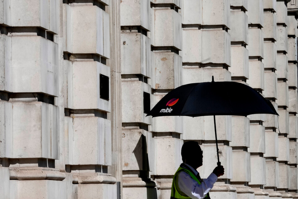 En vakt skuggar sig med ett paraply i London. Bild från augusti.