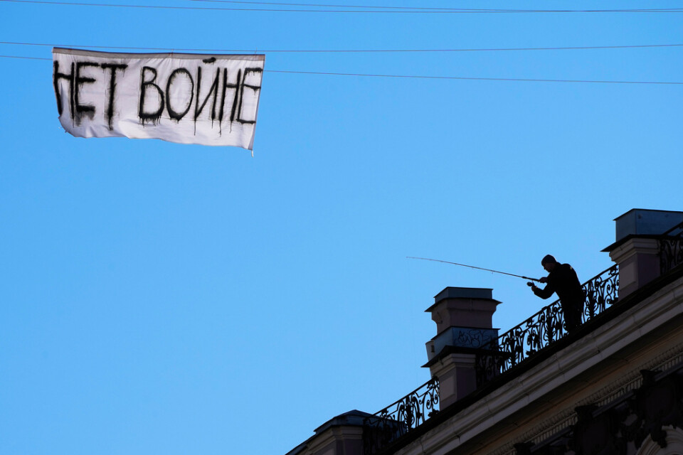 En man försöker med ett fiskespö ta ned en banderoll med texten "Inget krig" som hänger över en gata i centrala S:t Petersburg.