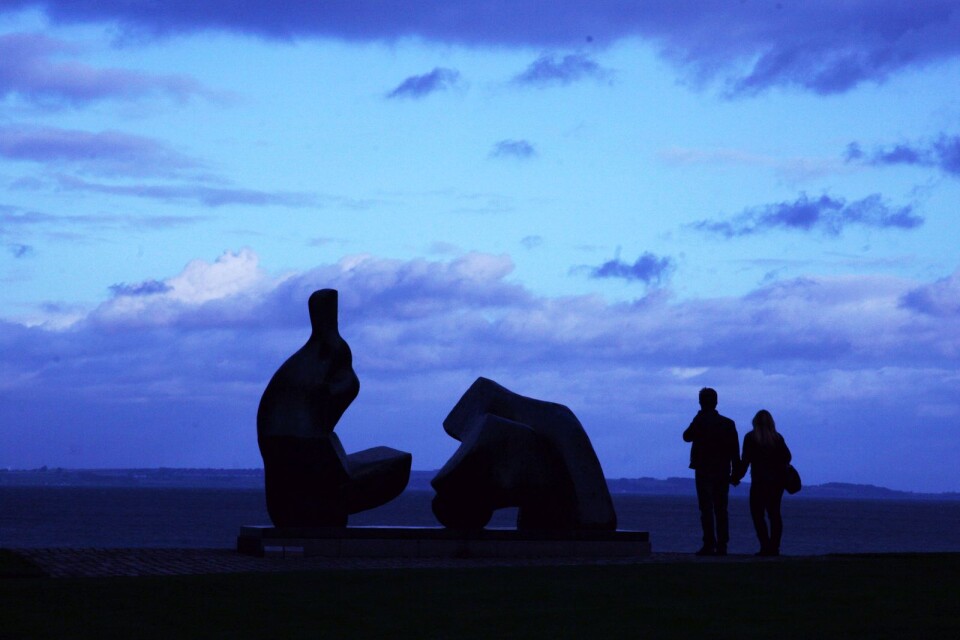 Två besökare bredvid den stora skulpturen av Henry Moore medan skymningen sänker sig över Öresund.