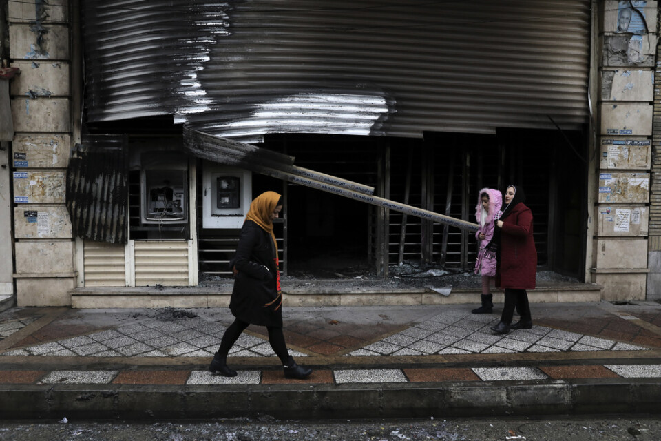 Lokalbor passerar förbi en bank i Shahriar i norra Iran som brandhärjats under protesterna. Arkivbild.