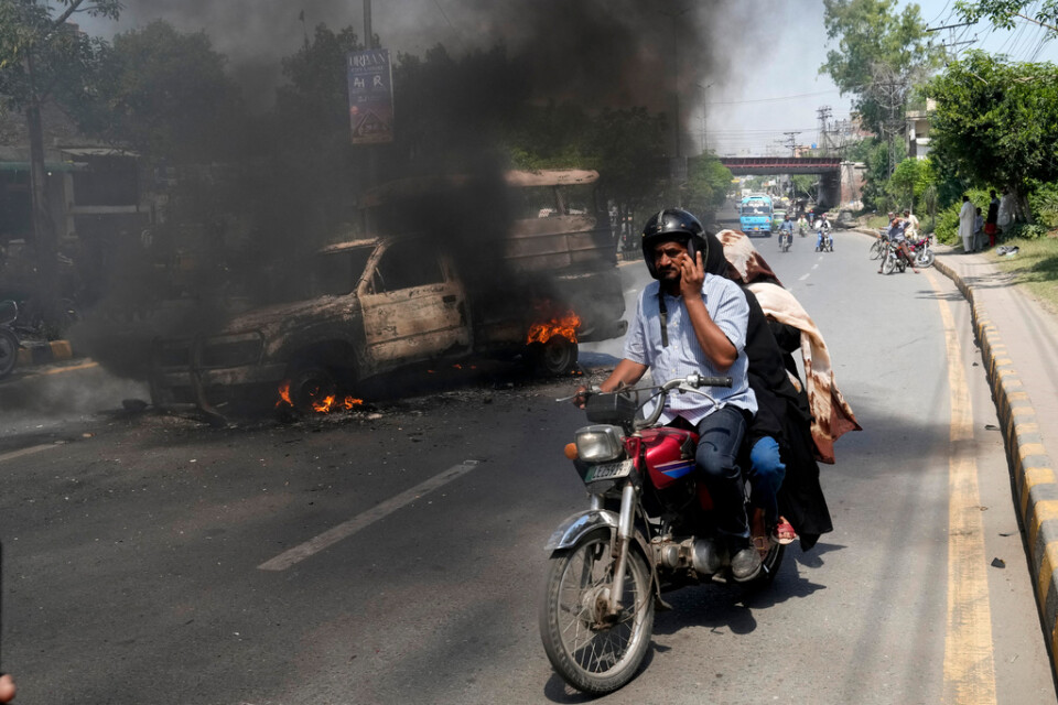 En motorcyklist kör förbi en bil som satts i brand av anhängare till Imran Khan i Lahore på torsdagen.
