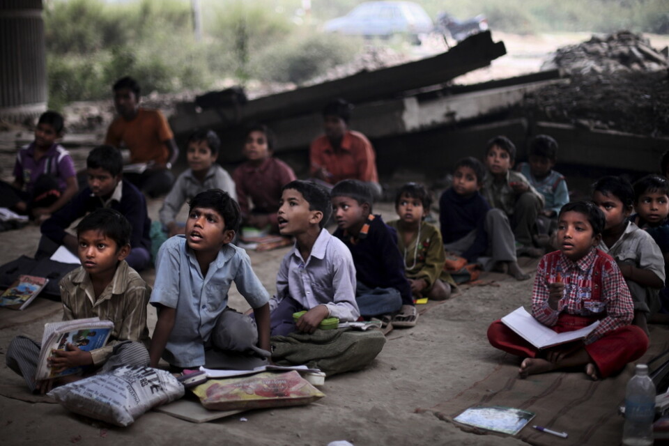 Barn från slumkvarter i Delhi får gratis skolundervisning under en bro. Arkivbild.