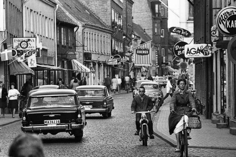 Stora Östergatan tidigt 1960-tal och bilarna kör på vänster sida som sig bör. Bilden är tagen i höjd med Apgränd i riktning mot Österports torg. På höger sida skymtar ni Denco-baren, en klassiskt samlingspunkt för Ystads unga. De flesta av butikerna finns inte längre. Andra, som Öbergs, hittar vi i dag på annan adress i Ystad.