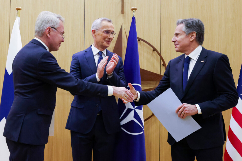 Finlands utrikesminister Pekka Haavisto skakar hand med USA:s utrikesminister Antony Blinken efter att ha överlämnat Finlands anslutningsdokument till Nato. Natos generalsekreterare Jens Stoltenberg applåderar.