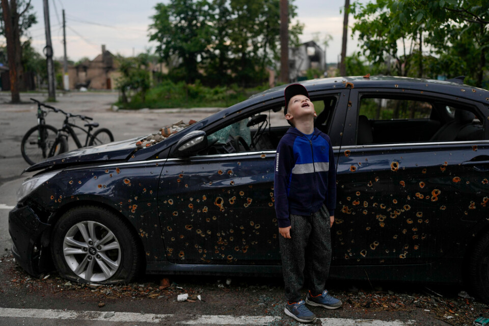 Ett barn tittar upp på ett förstört lägenhetshus i Irpin, i utkanten av Kiev. Bakom honom står en sönderskjuten bil. Bilden togs i måndags.