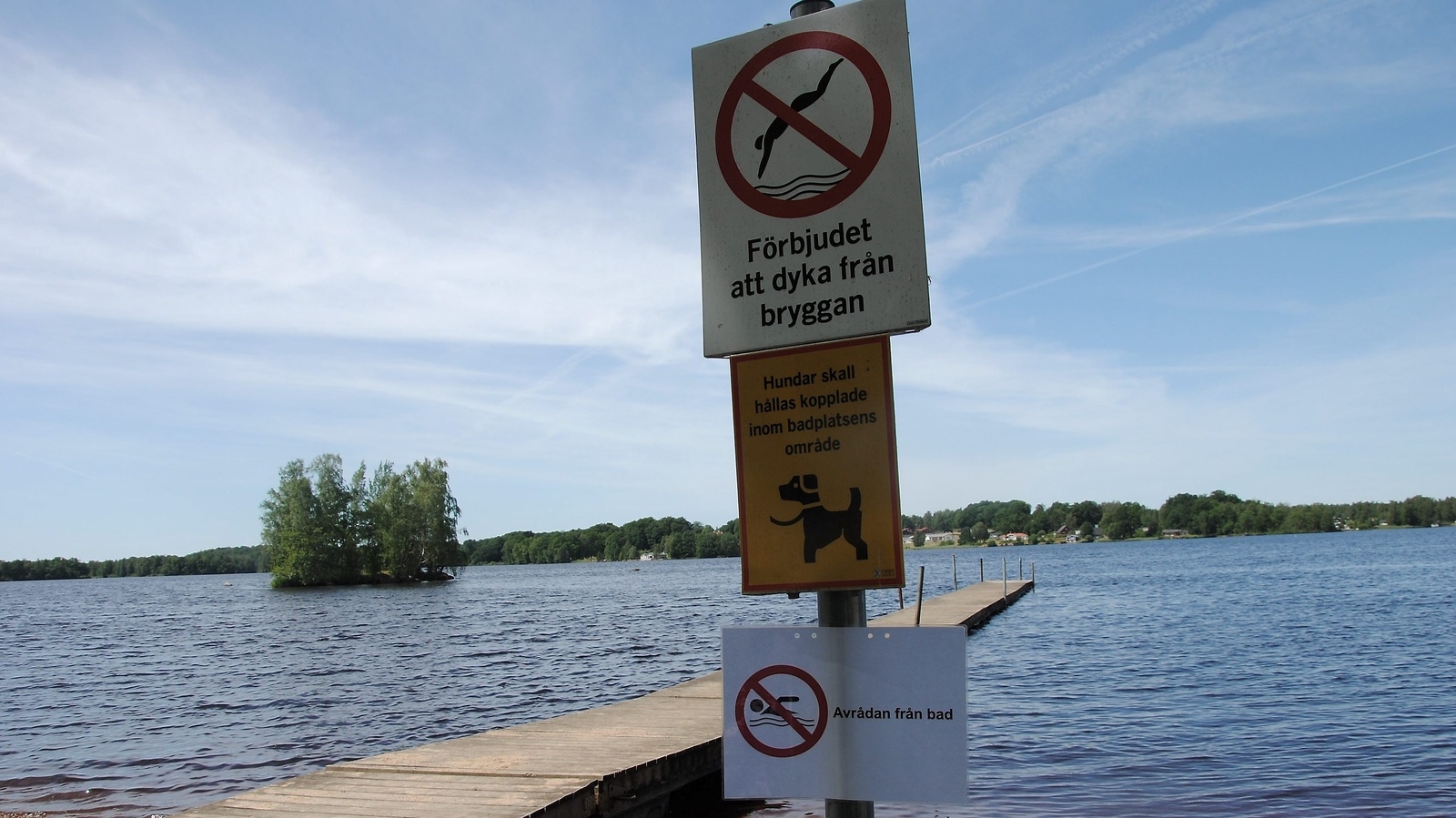 En lapp fladdrar i vinden med texten Avrådan från bad och inte en människa badar i Osbysjön.                                    FOTO: SUSANNE GÄRE