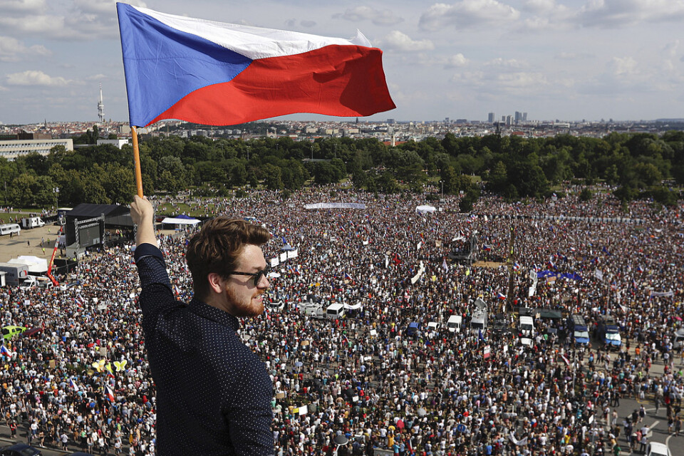 En man håller i den tjeckiska flaggan. I bakgrunden syns de tusentals demonstranter som samlats i Tjeckiens huvudstad Prag för att kräva premiärministerns avgång.