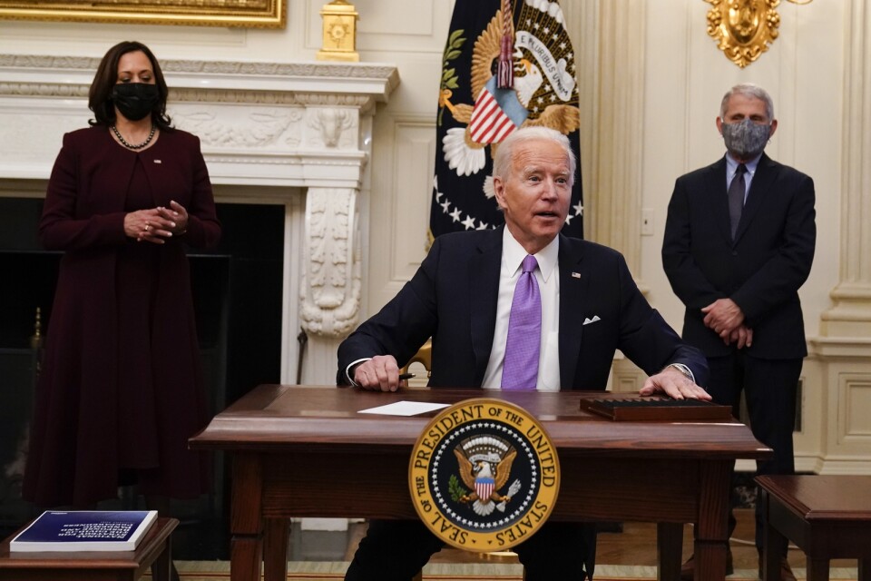 Joe Biden skriver under dekret i Vita huset. I bakgrunden står vicepresident Kamala Harris och smittskyddsexperten Anthony Fauci.