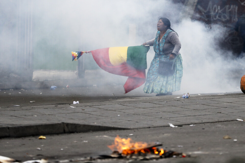 En anhängare till den avgångne presidenten Evo Morales demonstrerar i tårgas med en boliviansk flagga, med en flagga som representerar ursprungsbefolkningen ovanpå.