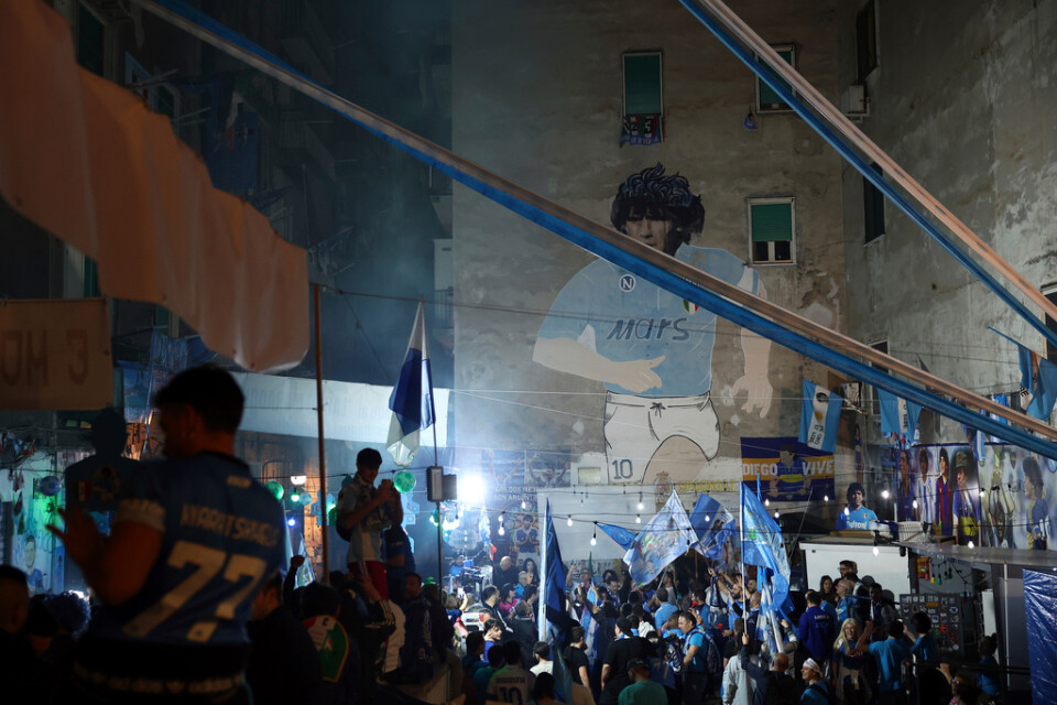 Napolifans firar framför en väggmålning föreställande Diego Maradona.