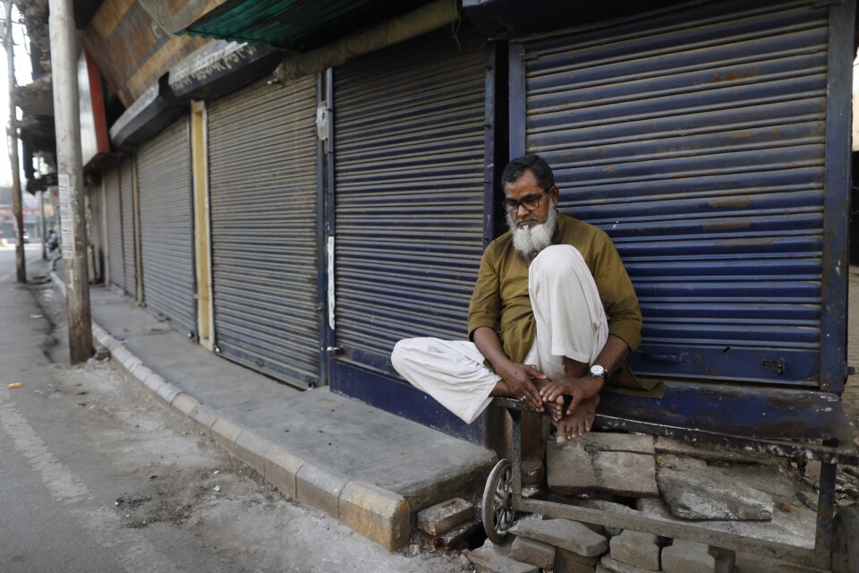En indisk man sitter framför en stängd butik i Prayagraj i Indien.