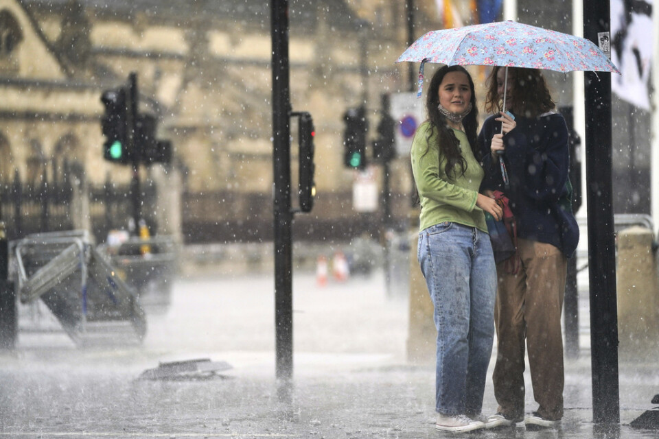 Två kvinnor tar skydd under ett paraply vid Parlamentstorget i centrala London. Kraftiga skyfall har drabbat huvudstaden.