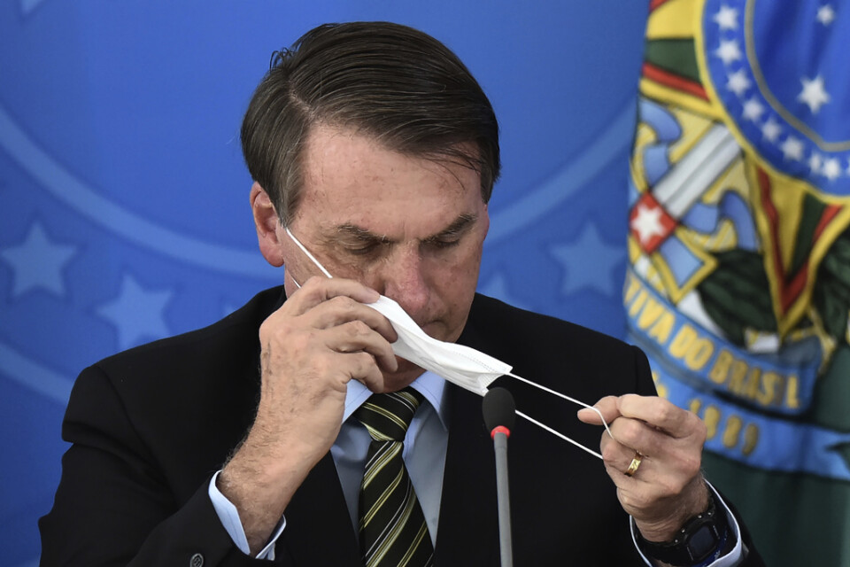 Brasiliens president Jair Bolsonaro provar en ansiktsmask under en presskonferens i fredags.