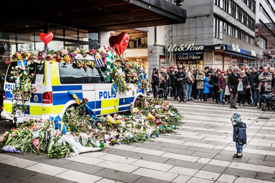 Ett litet barn tittar på alla blommor som täcker en polisbil utanför varuhuset Åhléns dagarna efter dådet.